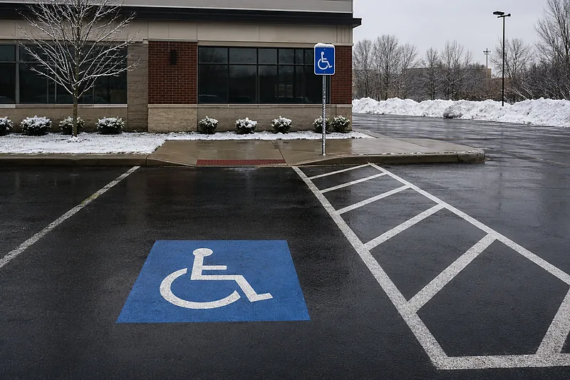 Accessible parking stall cleared to bare asphalt with the blue wheelchair symbol and the diagonal-striped access aisle beside it also clear, plowed snow banked well away at the lot edge