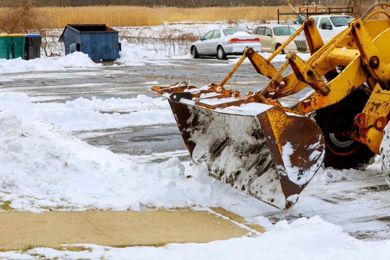 Wheel loader with a raised bucket working across a snow-covered commercial lot