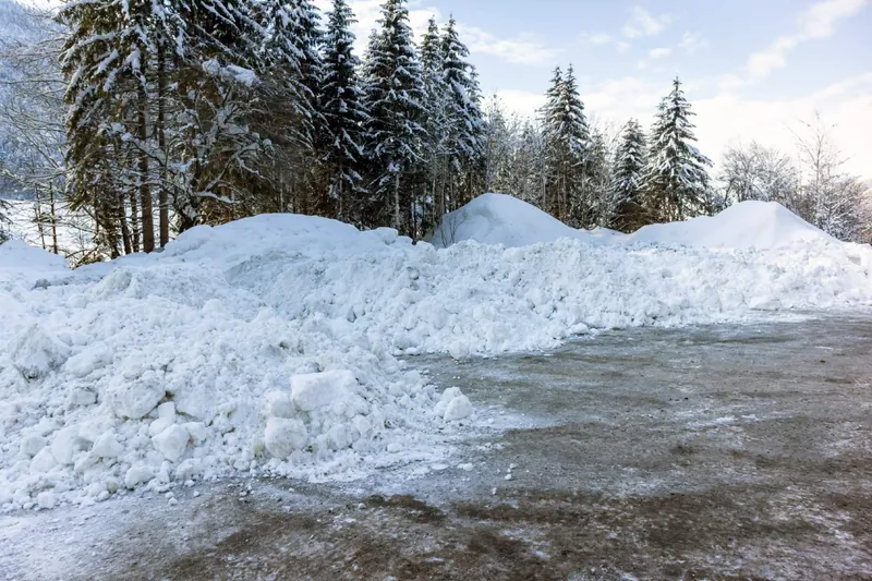 Large plowed snow piles heaped at the edge of a commercial parking lot, clear of the drive lanes