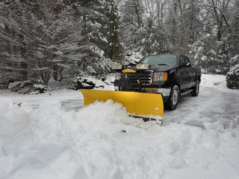 Three-quarter-ton pickup truck fitted with a yellow V-plow blade, parked in deep snow