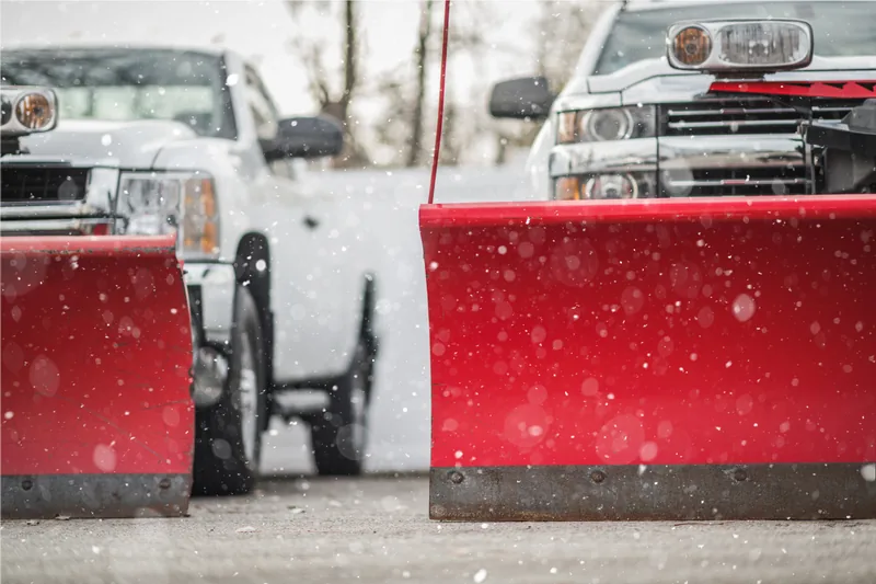 Row of pickup trucks fitted with red plow blades, staged and waiting as snow falls