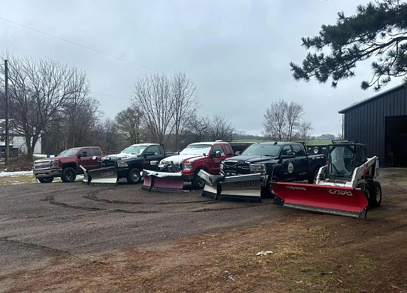 Row of pickup trucks fitted with plow blades staged in a lot before a storm
