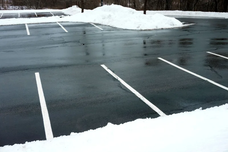 Commercial parking lot plowed down to bare wet asphalt with painted stall lines showing and plowed snow banked along the far edge