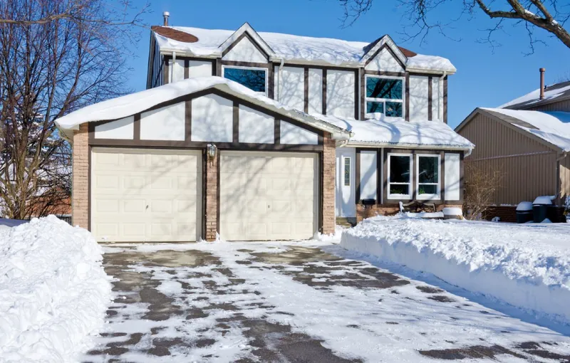 A cleared driveway at a two-car garage home with snow banked on both sides
