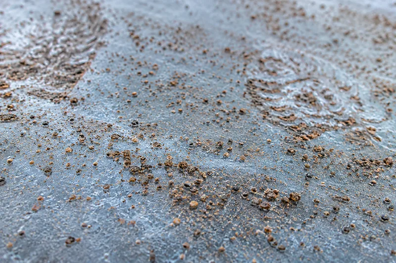 Coarse brown sand scattered for traction across a hard glassy layer of ice, the grit sitting on the surface with boot prints pressed into it