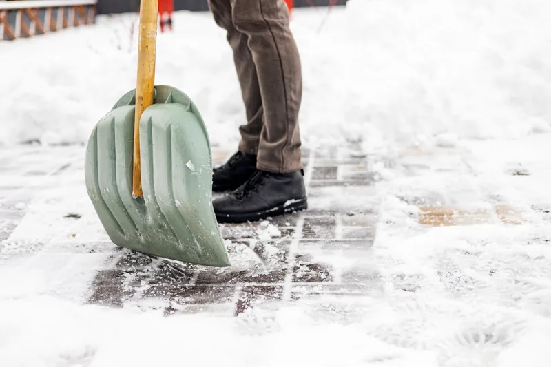 Close-up of a snow shovel clearing packed snow from a paved residential walkway
